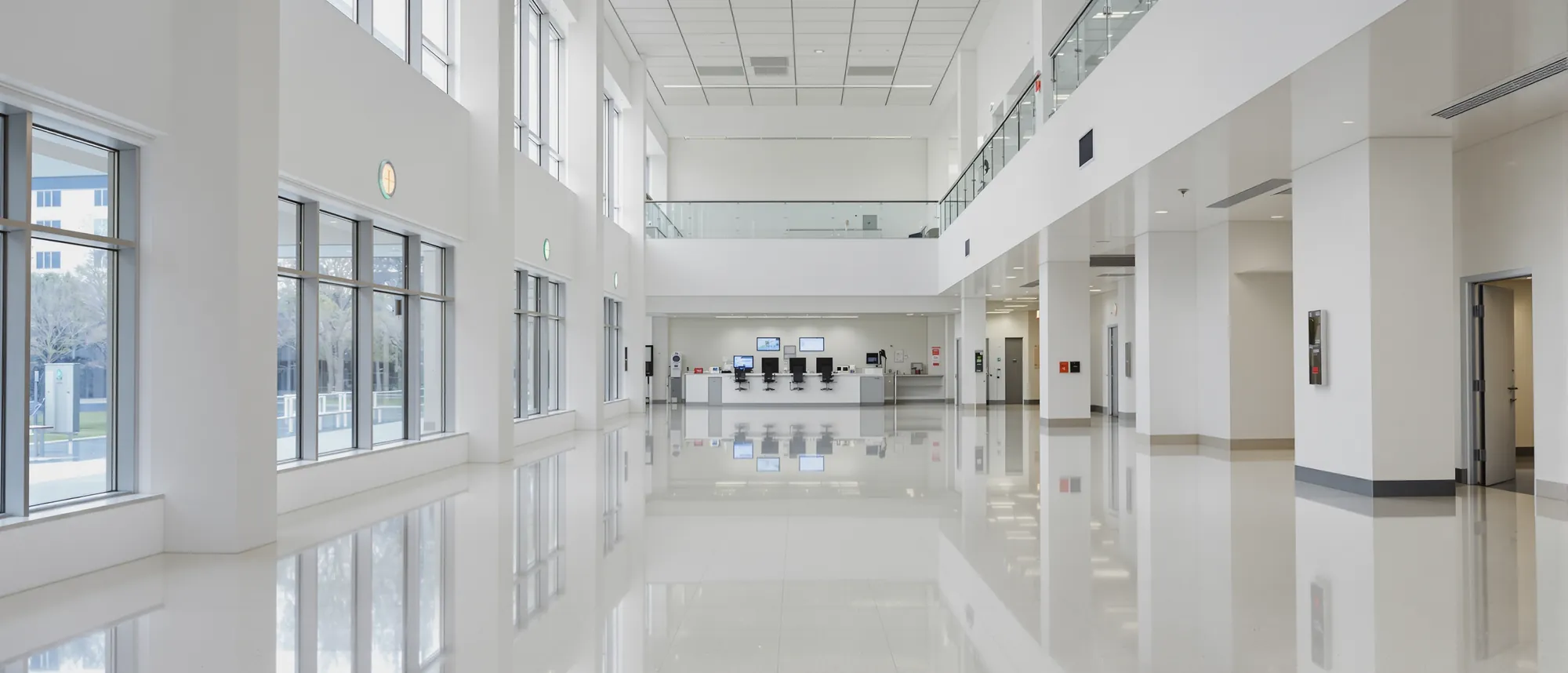 A bright, empty hospital atrium with tall windows, a nurses' station and a polished floor