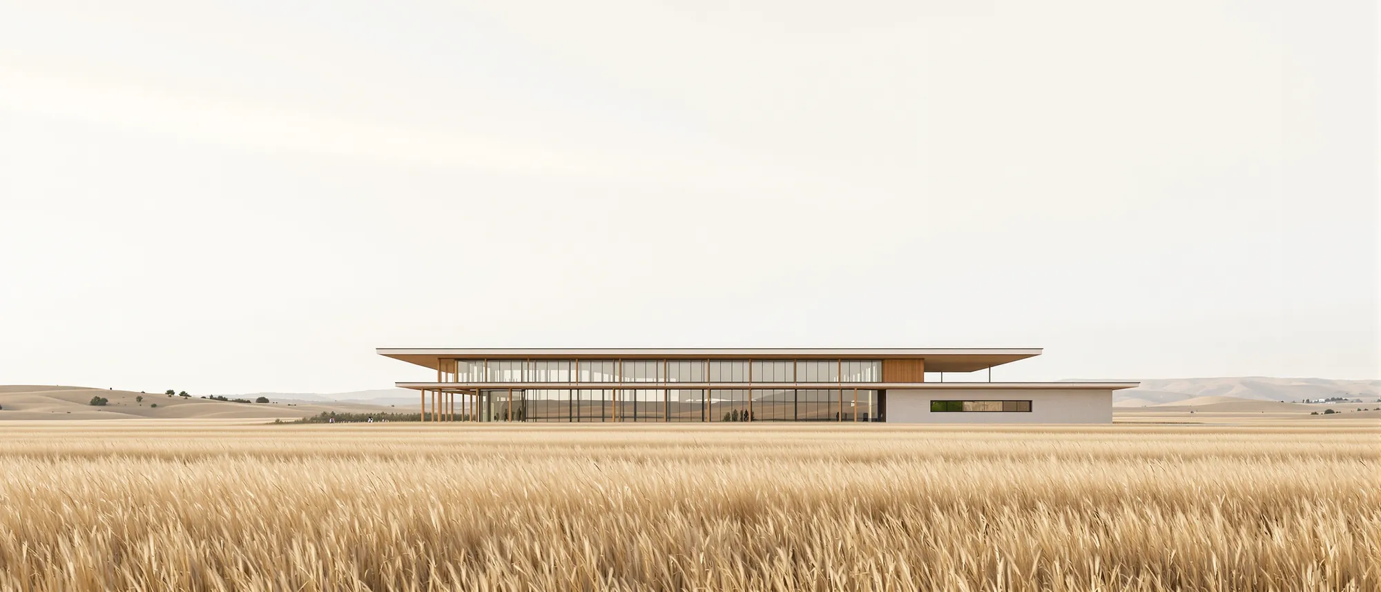 A low modern civic building of glass and timber in a wide prairie of tall golden grass under a pale sky